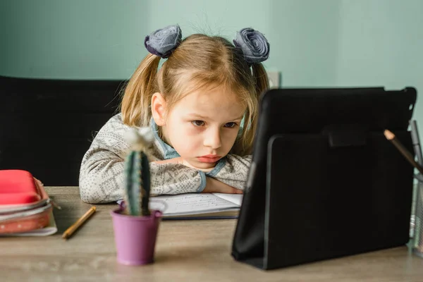 Moe schoolmeisje leunend op haar armen tijdens het hebben van online les thuis — Stockfoto