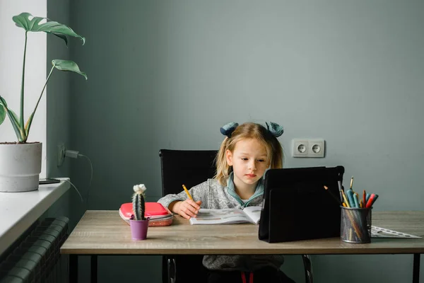 Klein meisje kijken video les op haar tablet en schrijven in haar notebook — Stockfoto