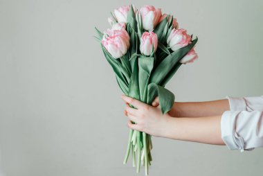 Yeşil arka planda bir demet pembe lale tutan eller, Kadınlar Günü tebrik kartı.