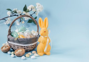 Sarı Paskalya tavşanlı Paskalya kompozisyonu ve mavi arka planda renkli Paskalya yumurtaları.
