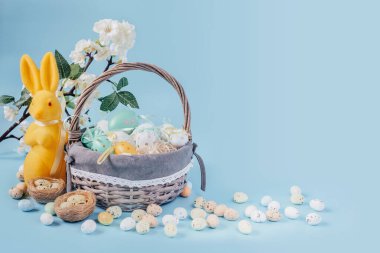 Sarı Paskalya tavşanlı Paskalya kompozisyonu ve mavi arka planda renkli Paskalya yumurtaları.