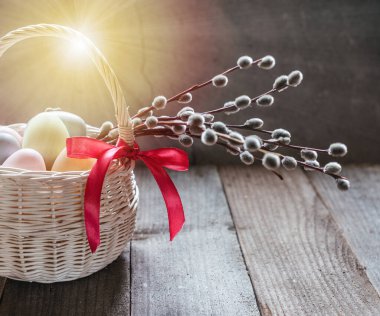 Easter basket with colorful Easter eggs and pussy willow branches on wooden background. Happy Easter greeting card.