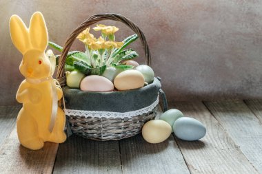 Paskalya arkaplanı, sarı Paskalya tavşanı, renkli yumurtalar ve sarı menekşe çiçekleriyle dolu bir sepet..