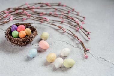 Kuşlarda renkli Paskalya yumurtaları. Gri çimento arka planında süs ağacı dalları var.
