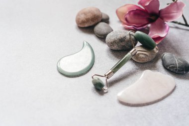 Yüz masajı aletleri: çakıl taşları ve mor manolya çiçekli yeşim taşlı kazıyıcı, SPA rahatlama, yüz bakımı ve cilt bakımı