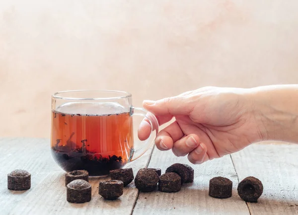 Bir bardak geleneksel Çin porsuğu çayını tutan bir el. Ahşap arka planda eski puerh çay tuğlaları, pu-erh kese demleme.