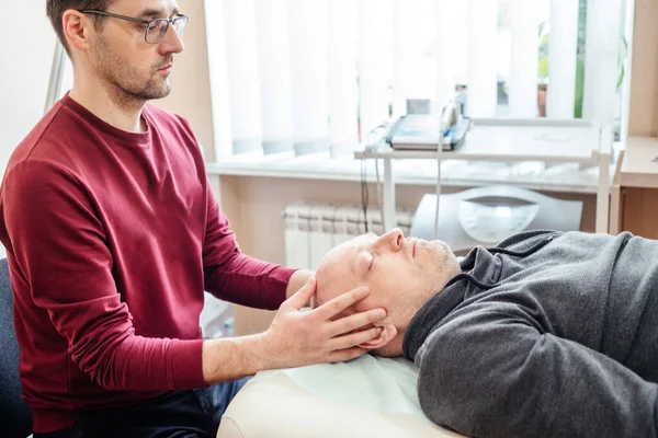Kraniosakral terapi uygulayıcısı erkek bir hastaya CST osteopati, osteopati ve manüel terapi uyguluyor.