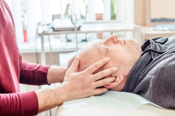Kraniyal sakral terapi gören erkek hasta, CST osteopatik kliniğindeki masaj masasında yatıyor, osteopati ve manuel terapi görüyor.