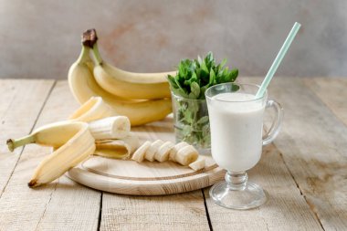 Sütlü kahve bardağında yoğurt muzlu milkshake. Nane yapraklı ve muz saplı. Tahta arka planda, yaz içkileri.