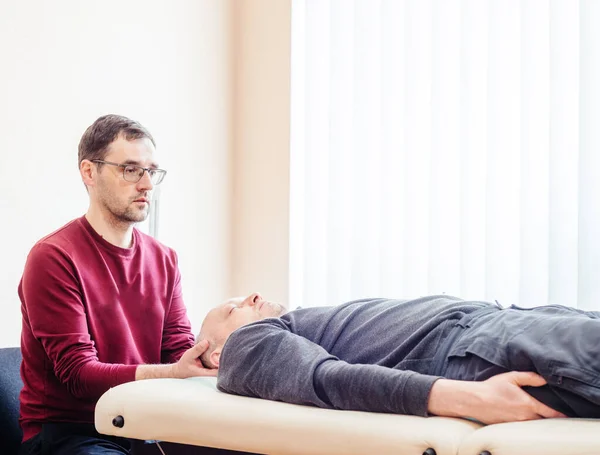 Kraniyal sakral terapi gören erkek hasta, CST osteopatik kliniğindeki masaj masasında yatıyor, osteopati ve manuel terapi görüyor.