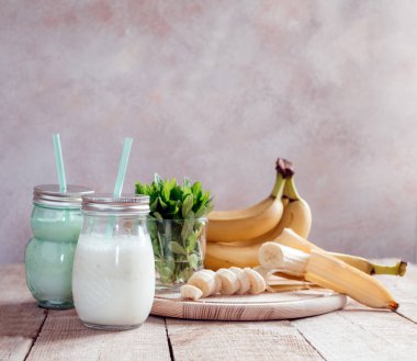 Yaz muzlu smoothie veya naneli milkshake ve siyah ahşap masadaki kavanozlarda saman.