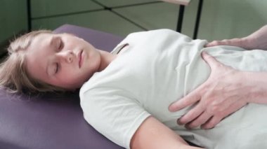 Osteopat pratisyen kadın bir hastanın diyaframını salıyor, göğüs kafesi masajı yapıyor, kas gevşetici soluyor.