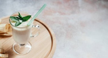 Süt muzlu milkshake latte bardakta nane yaprağı ile süslenmiş ve arka planda fotokopi alanı ve yaz içecekleriyle dolu.