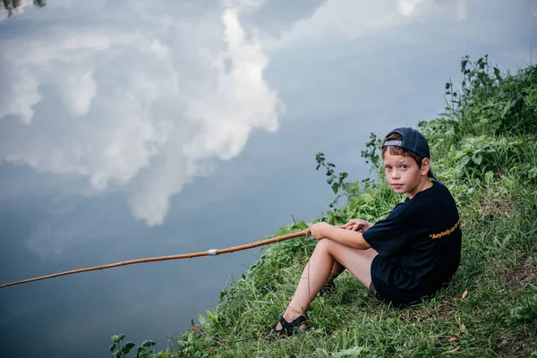 Un niño sosteniendo una caña de pescar y la pesca en el lago, actividades de verano y pasatiempos para los niños — Foto de Stock