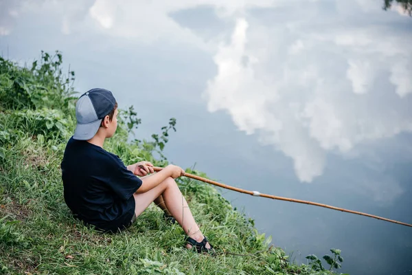 Un niño sosteniendo una caña de pescar y la pesca en el lago, actividades de verano y pasatiempos para los niños — Foto de Stock