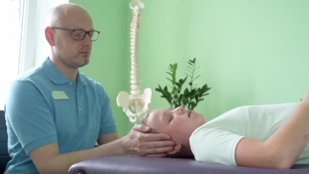 Uma menina que recebe tratamento CST por praticante de osteopata usando a técnica hands-on suave, tensão do sistema nervoso central aliviar — Vídeo de Stock