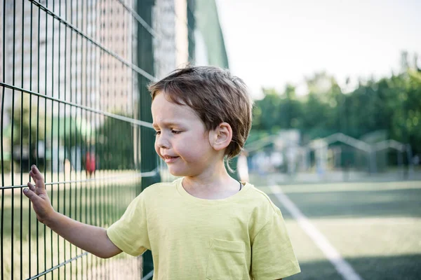 Llorando infeliz niño sosteniendo la valla de metal, estresado y molesto niño pequeño no quiere ir a la escuela — Foto de Stock