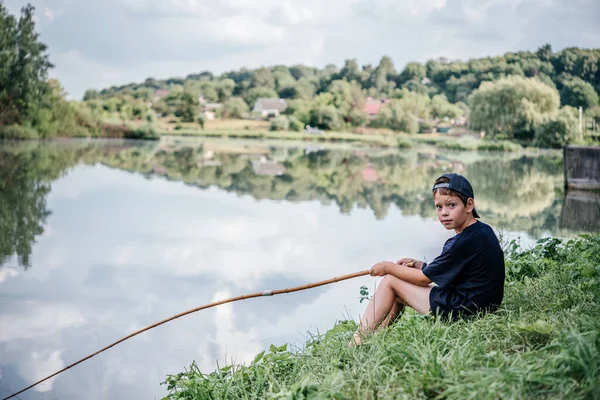 Un niño sosteniendo una caña de pescar y la pesca en el lago, actividades de verano y pasatiempos para los niños — Foto de Stock