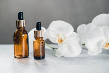 Arka planda orkide çiçekleri olan serum ya da temel yağ şişesi modeli, doğal güzellik kozmetik ürünleri, damlatan şişedeki spa.