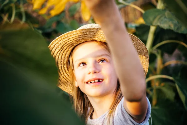 Niña en un sombrero de paja jugando en el campo de girasol, niños entre los girasoles fondo de verano — Foto de Stock