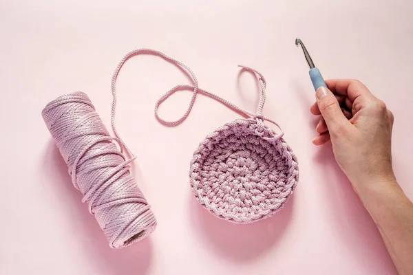 A hand holding a crochet hook and pink color yarn on a pink background, knitting and crochet supplies, hobby and craft — Stock Photo, Image