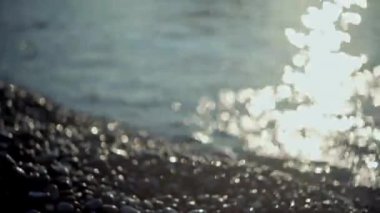 Çakıl taşı plajında kıvılcımlar saçan su damlalarıyla deniz yüzeyinde parlak ışık izleri.