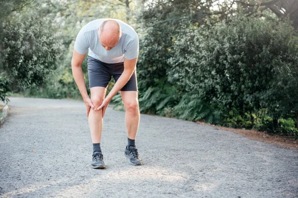 Mężczyzna biegacz trzyma kolano i cierpi z powodu kontuzji kolana biegaczy — Zdjęcie stockowe