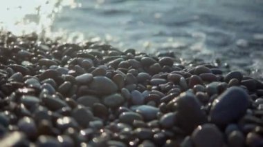 Köpüklü dalgalar çakıl taşlı sahile vuruyor.