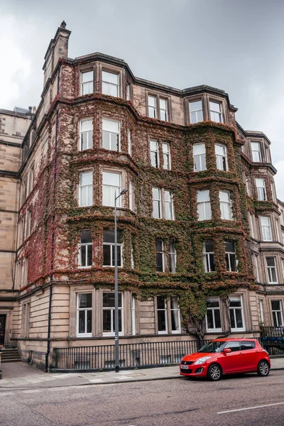 Edinburgh İskoçya 'da geleneksel taş bina sarmaşık kaplı cephe ve sokağa park etmiş kırmızı bir araba, şehir mimarisini ve mevsimsel değişimi gösteriyor.