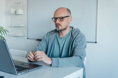 Modern bir ev ofisinde dizüstü bilgisayarda çalışan kel, orta yaşlı bir adam. Odaklanmış ve ciddi. Uzaktan çalışma, teknoloji ve iş kavramları için uygun.