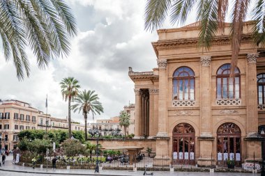 Palermo, Sicilya 'daki tarihi Teatro Politeama Garibaldi tiyatrosu dramatik bulutlar altında palmiye ağaçları ve şehir meydanı mimarisi ile çevrili, İtalyan kültürünü, seyahat merkezlerini ve Akdeniz kentsel turizmini temsil ediyor.