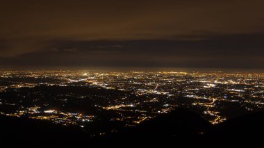 Elektrik ışığıyla aydınlatılmış bir düzlüğün havadan görünüşü. Grappa Dağı, İtalyan manzarası