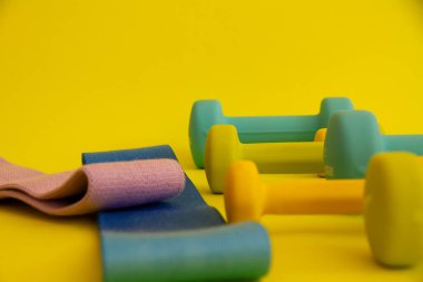 Sarı arka planda mavi halterler. Spor malzemeleri. Bacakları şişirmek için farklı renklerde dambıllar.