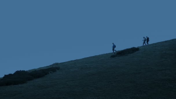 夕暮れ時に丘の中腹を歩く人々のハイカーグループ — ストック動画