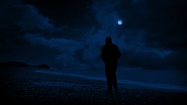 Adam sahilde yürür ve gece dışarı bakar.