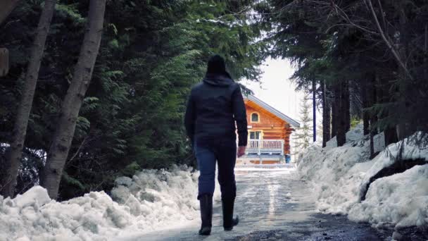 Человек подходит к дому в снежном лесу — стоковое видео