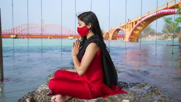 Indian Woman meditera bär Coronavirus skydd ansiktsmask sitter i Sadhana eller andlig position på klippa över heliga floden Ganges, Haridwar Uttarakhand Indien, Appleprores 422 Cinetone 4k — Stockvideo