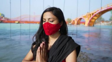 Coronavirus maskesi takan Hintli kadın Sadhana 'da oturuyor veya Ganj nehrinin üzerindeki kayanın üzerinde ruhani pozisyonda oturuyor, Haridwar Uttarakhand Hindistan, Appleprores 422 Cinetone 4k 