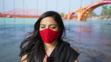 Coronavirus maskesi takan Hintli kadın Sadhana 'da oturuyor veya Ganj nehrinin üzerindeki kayanın üzerinde ruhani pozisyonda oturuyor, Haridwar Uttarakhand Hindistan, Appleprores 422 Cinetone 4k 