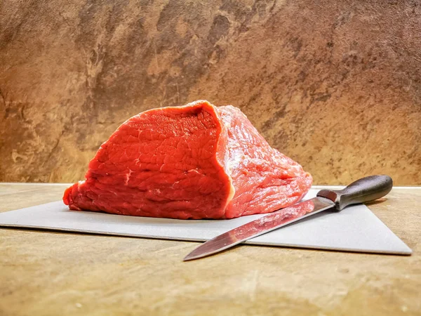 Yanında bir bıçakla kesme tahtasının üzerinde taze kesilmiş kırmızı et parçası.
