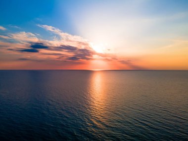 Dalgalanan denizin üzerinde bulutlar arasında güzel renkli bir gün batımı.