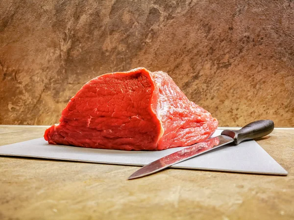 Yanında bir bıçakla kesme tahtasının üzerinde taze kesilmiş kırmızı et parçası.