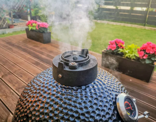 Kamado yumurtalı barbekü ızgarası. Oturma odasının terasında duruyor. Bacasından çıkan dumanla birlikte.