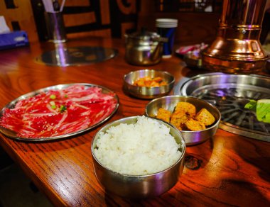 Masasında tabaklar olan Kore barbekü restoranı. Geleneksel Kore yemeği, içinde ızgara var. Domuz eti ve sığır eti kömür ocağında ızgaraya hazır.