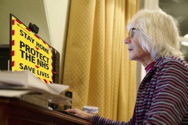 Bilgisayar monitöründe yeni koronavirüs kılavuzu okuyan yaşlı bir kadın.