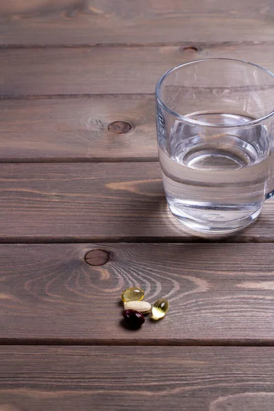 A glass of water and a daily vitamin complex on a wooden table. vertical snapshot