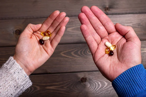 A man and a woman hold vitamins in their hands on a blurry wooden background. Vitamin capsules on the palms. Dietary supplements for human health.