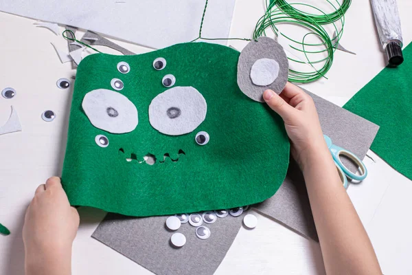 Hands of a child doing homework on making an alien mask. Craft tools, objects and accessories for creativity. Development of fine motor skills in children.