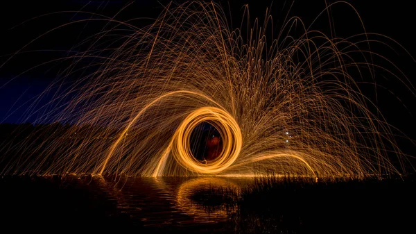 スチールウール紡糸 春の夜の風景の背景にある水湖の表面に火花を燃やす軌跡 — ストック写真