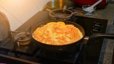 Kızartma tavasında yumurta krepleri pişirmek, gaz ocağının tepesinde tava yapmak. Görüntü gürültülü, odaklanma yumuşak..